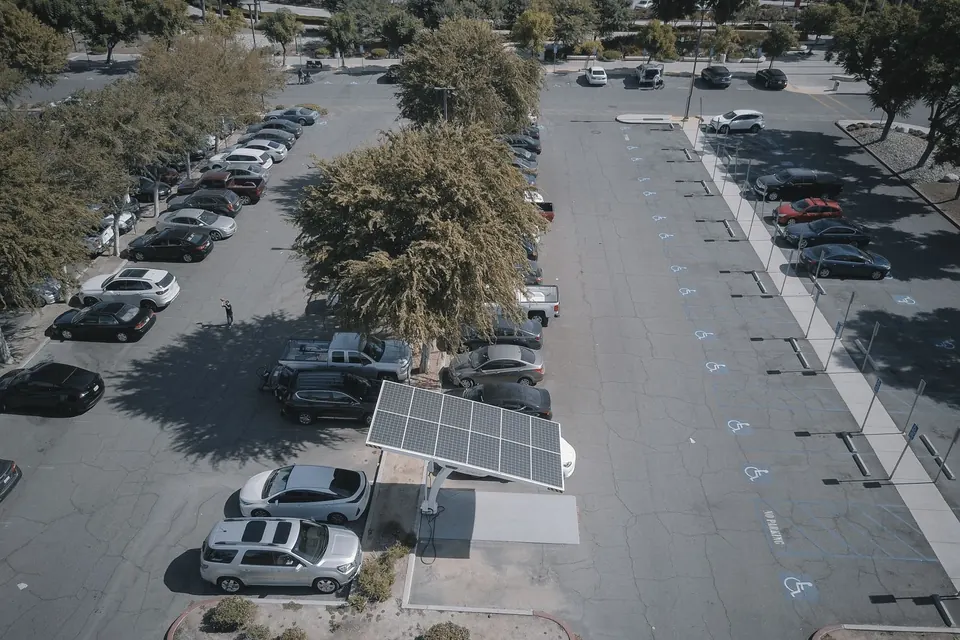 Aerial view of a solar panel charging station in a busy parking lot surrounded by cars and trees.